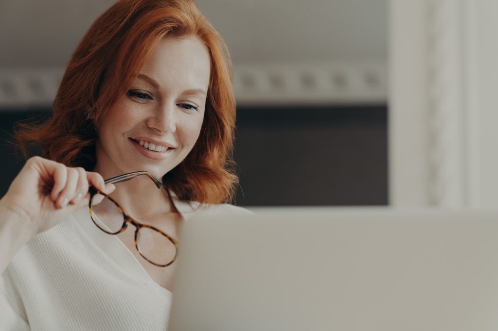 Photo of good looking cheerful redhead woman reads information on website in internet